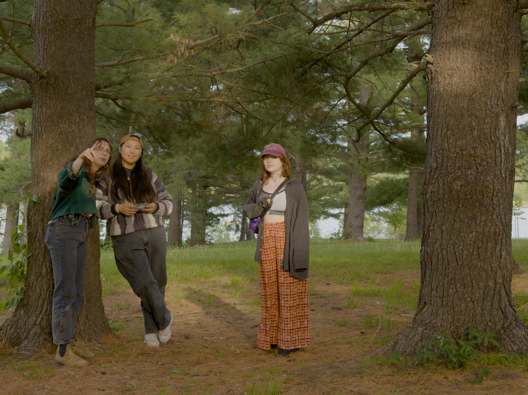 Three girls standing in grove of trees, one pointing.